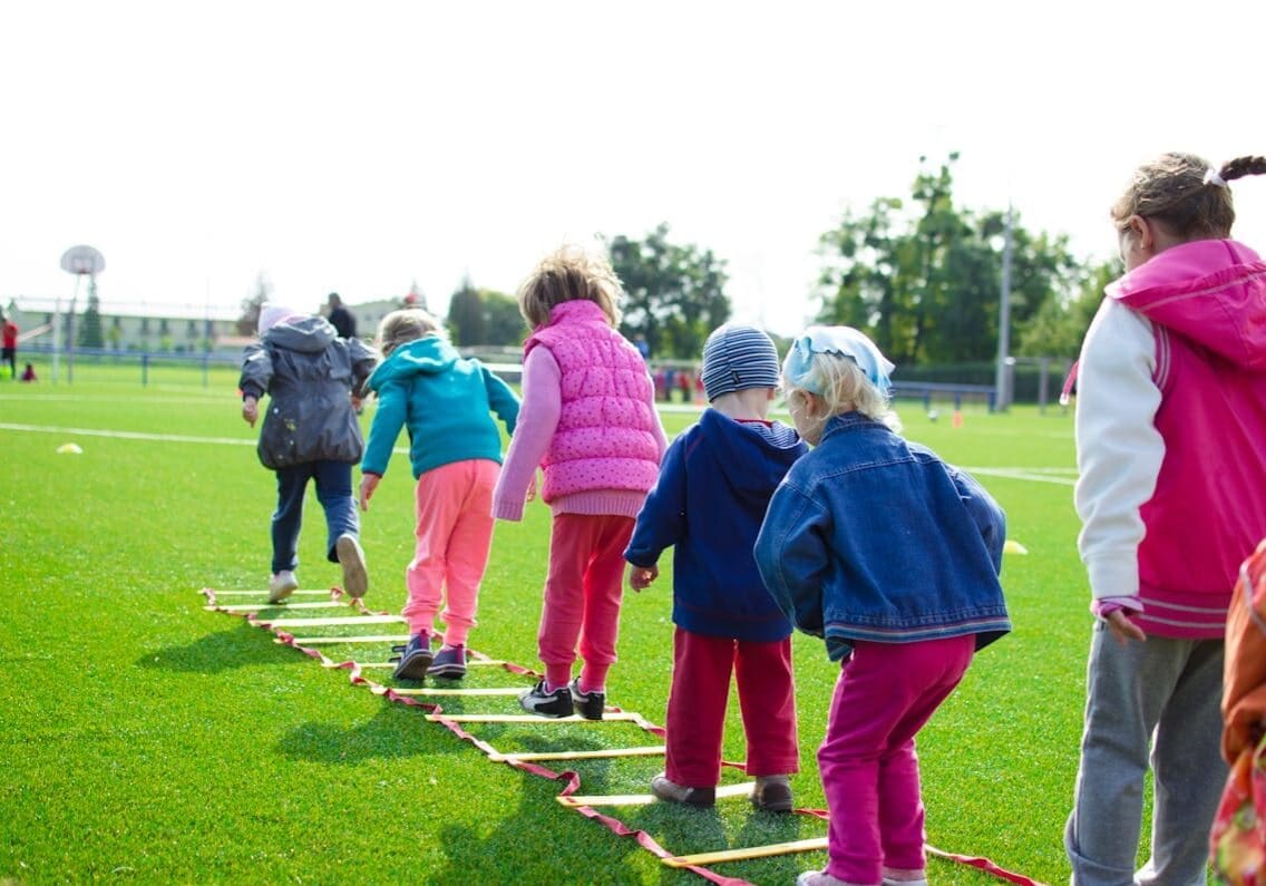 Children stepping through agility ladder on field